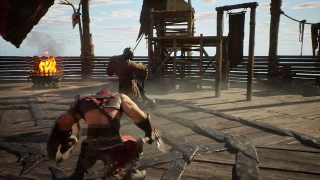Official trailer frame: two fighters trading blows on a wooden platform beside a fire pit